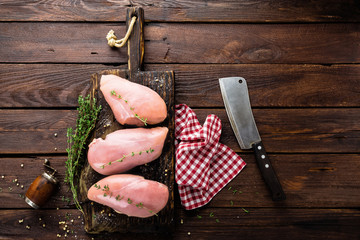 Raw chicken breasts fillets with thyme and spices on wooden cutting board on rustic background copy space directly above