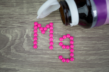 Wall Mural - Pink pills forming shape to Mg alphabet on wood background