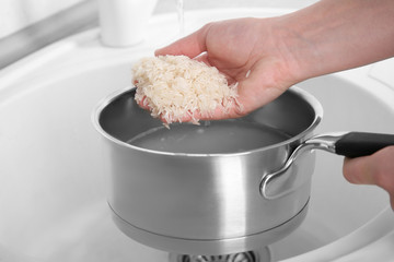 Canvas Print - Woman rinsing rice in saucepan with water