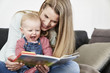 © Westend61 - Mother and happy baby girl at home looking at book