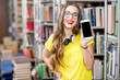 © rh2010 - Young smiling student showing smart phone with empty screen standing at the library. Mobile application concept