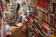 © rh2010 - Young woman student sitting on the heap of books at the old library
