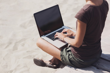 Wall Mural - Young woman using laptop computer on a beach. Freelance work concept