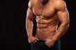 © satyrenko - Strong Athletic Man - Fitness Model showing Torso with six pack abs. stands straight and puts his hands in trousers. isolated on black background with copyspace