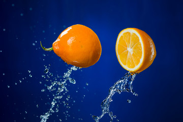 two halves of orange and splash of water on blue background