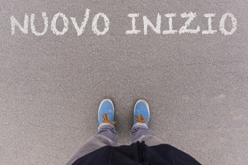 Wall Mural - Nuovo inizio, Italian text for New Beginning text on asphalt ground, feet and shoes on floor