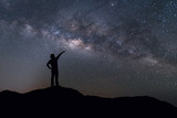 Fototapeta Kosmos - Milky Way landscape. Silhouette of Happy woman standing on top of mountain with night sky and bright star on background.