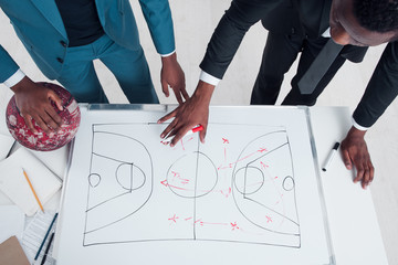 Two african basketball coaches plan and discuss new game strategy. Trainers making scheme of basketball game on the white board.