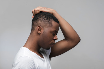 Thoughtful young african american guy looking down on grey background. Finding way to solve problems with free space for text.