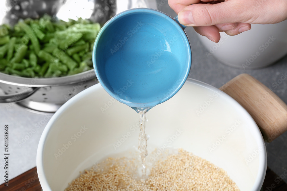 Female hand pouring water into saucepan with quinoa seeds