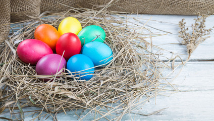 Colorful easter eggs in hay on wooden background