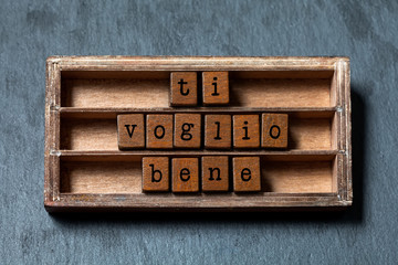 Wall Mural - Ti voglio bene. I love you written in Italian translation. Vintage box, wooden cubes phrase with old style letters. Gray stone textured background. Close-up, up view, soft focus