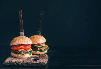 Two mouth-watering, delicious homemade burger used to chop beef. on the wooden table. The burgers are inserted knives.