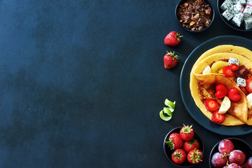 Healthy breakfast with homemade crepes with strawberries, grapes, dragon fruit, golden kiwi and honey over black background with a copy space. 