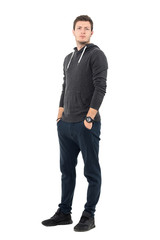 Wall Mural - Serious frowning man in sportswear with hands in pockets looking at camera. Full body length portrait over white studio background.