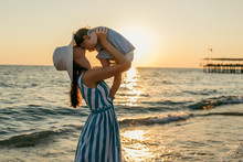 Beautiful Young Mother Kiss Daughter At The Sea Sunset And Beach Background. Happy Family Vacation. Travel. Caucasian Happy Female With Baby Outside At Ocean Sunset. Motherhood Love Care. Silhouette