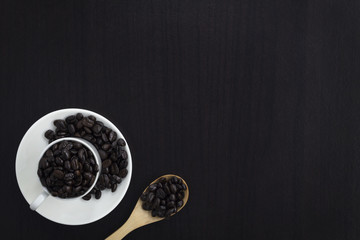 Wall Mural - cup of coffee beans with wood spoon on black wooden table.