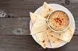 Hummus dip with pita bread on a plate, above view on a rustic wooden background