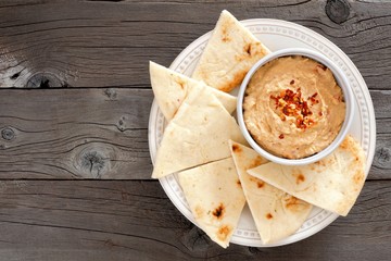 Wall Mural - Hummus dip with pita bread on a plate, above view on a rustic wooden background