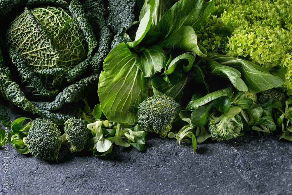 Variety of raw green vegetables salads, lettuce, bok choy, corn, broccoli, savoy cabbage as frame over black stone texture background. Space for text - obrazy, fototapety, plakaty 