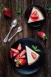 Strawberry cheesecake on black plate over rustic wooden background. Top view