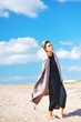 © raisondtre - Fashion shot on the beach. Attractive elegant woman in a black dress and coat. Girl posing in fashionable clothes for advertising on background of blue sky.