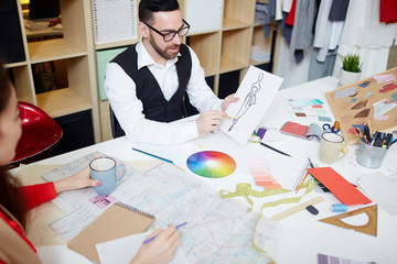 Confident man pointing at fashion sketch on paper while interacting with colleague