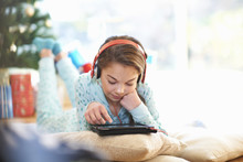 Girl Lying On Living Room Floor Looking At Digital Tablet At Christmas