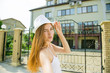 © NatBud - Street fashion concept. Outdoor fashion portrait of young pretty woman in summer sunny day on street. Portrait of a cheerful girl traveler. Young girl in a white hat walking the streets of the city
