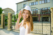 © NatBud - Street fashion concept. Outdoor fashion portrait of young pretty woman in summer sunny day on street. Portrait of a cheerful girl traveler. Young girl in a white hat walking the streets of the city