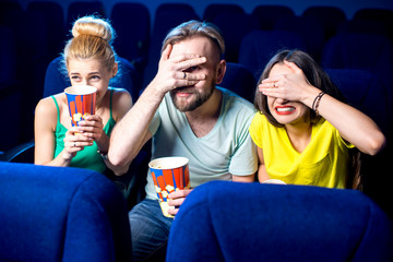 Scared friends watching film sitting together with popcorn in the cinema