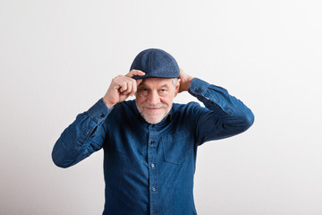 Wall Mural - Senior man in denim shirt and flat cap smiling, studio shot.