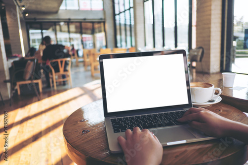 Fotomural Mockup image of a woman using laptop with blank white screen on wooden table in