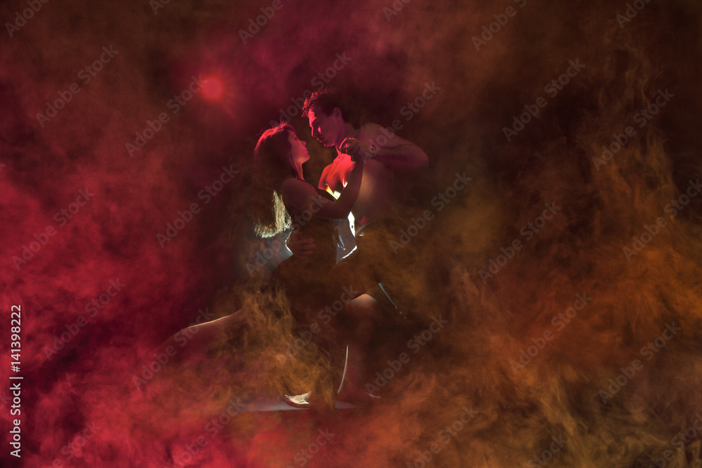 Young caucasian couple dancing tango in a burning room . Red backlight, low key image.  - obrazy, fototapety, plakaty 