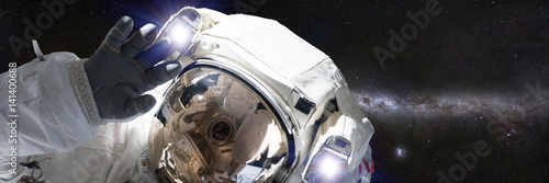 Zdjęcie XXL astronauta przed galaktyką Drogi Mlecznej machający kamerą (format bannera 3x1, elementy tego obrazu są dostarczane przez NASA)
