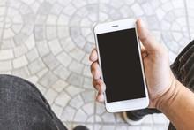 Mockup Image Of Hands Holding White Mobile Phone With Blank Black Screen, Soft-focus In The Background. Over Light And Film Colors Tone