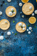 Lemon curd and blueberry jam tarts with meringue and basil leaves Chamomiles whole and slices of fresh lemon on a blue rusty textured background. Copy Space. Flat lay. Top View.