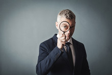 Businessman Looks At Us Through A Magnifying Glass