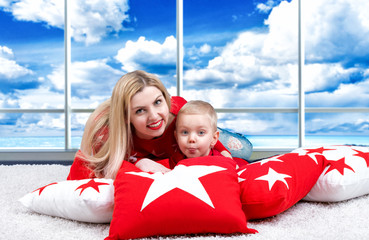 Young mother and little son playing lying on the pillow.         The concept of a family holiday. Beautiful cushions for home interior decorating.