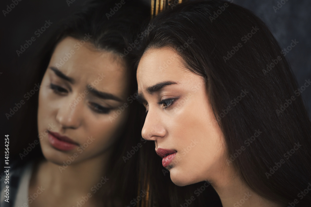 Depressed young woman and her reflection in mirror