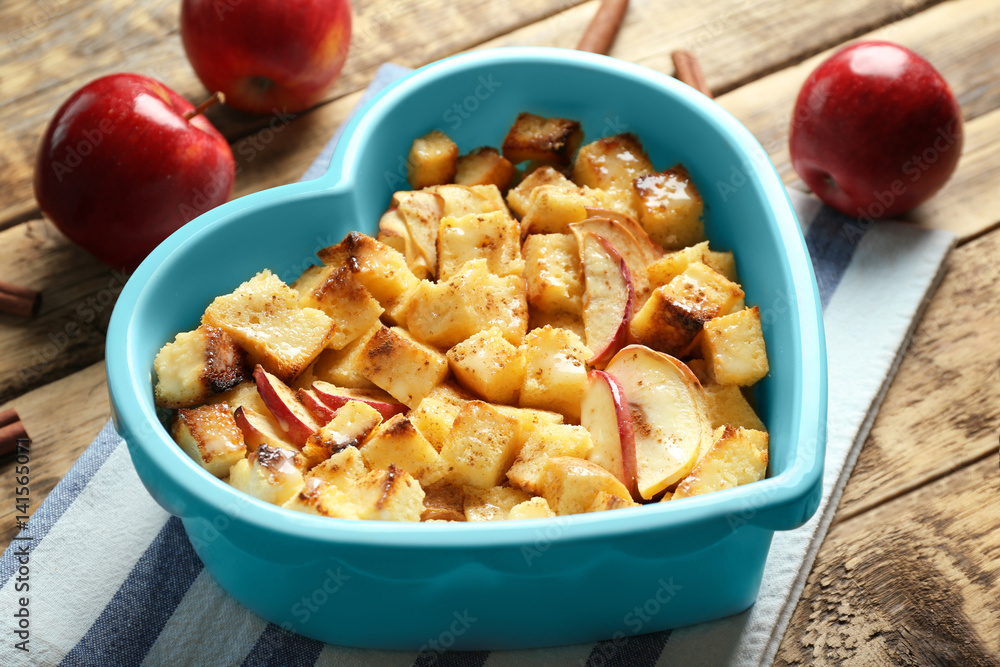 Delicious bread pudding with apples in heart shape bowl on table