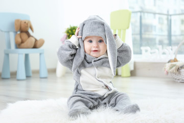 cute little baby in bunny costume sitting on furry rug at home
