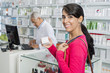 © Tyler Olson - Customer Holding Medicine Box While Chemist Working In Pharmacy