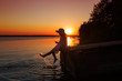 Little girl in a hat splashes her feet in the evening at sunset