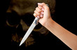 © zilvergolf - hand holding a knife ready to strike down against skull on black background