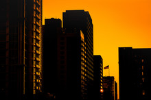 Silhouettes Of Buildings Against A Golden Sunset With American Flag