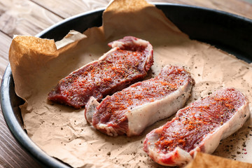 Canvas Print - Raw steaks with spices on parchment in baking dish