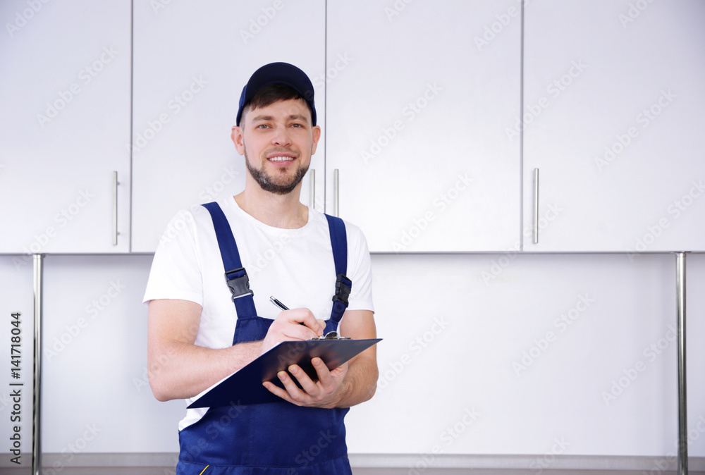 Plumber in uniform holding clipboard at kitchen