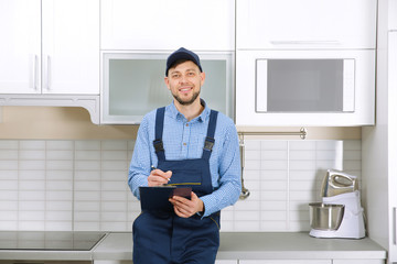 Wall Mural - Plumber in uniform holding clipboard at kitchen