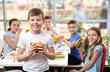© Africa Studio - Cute boy eating hamburger and children sitting at table in school cafeteria